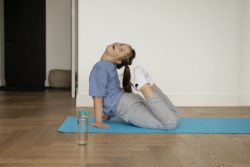una ragazzina con la sindrome di down pratica sorridendo lo yoga sul suo tappetino